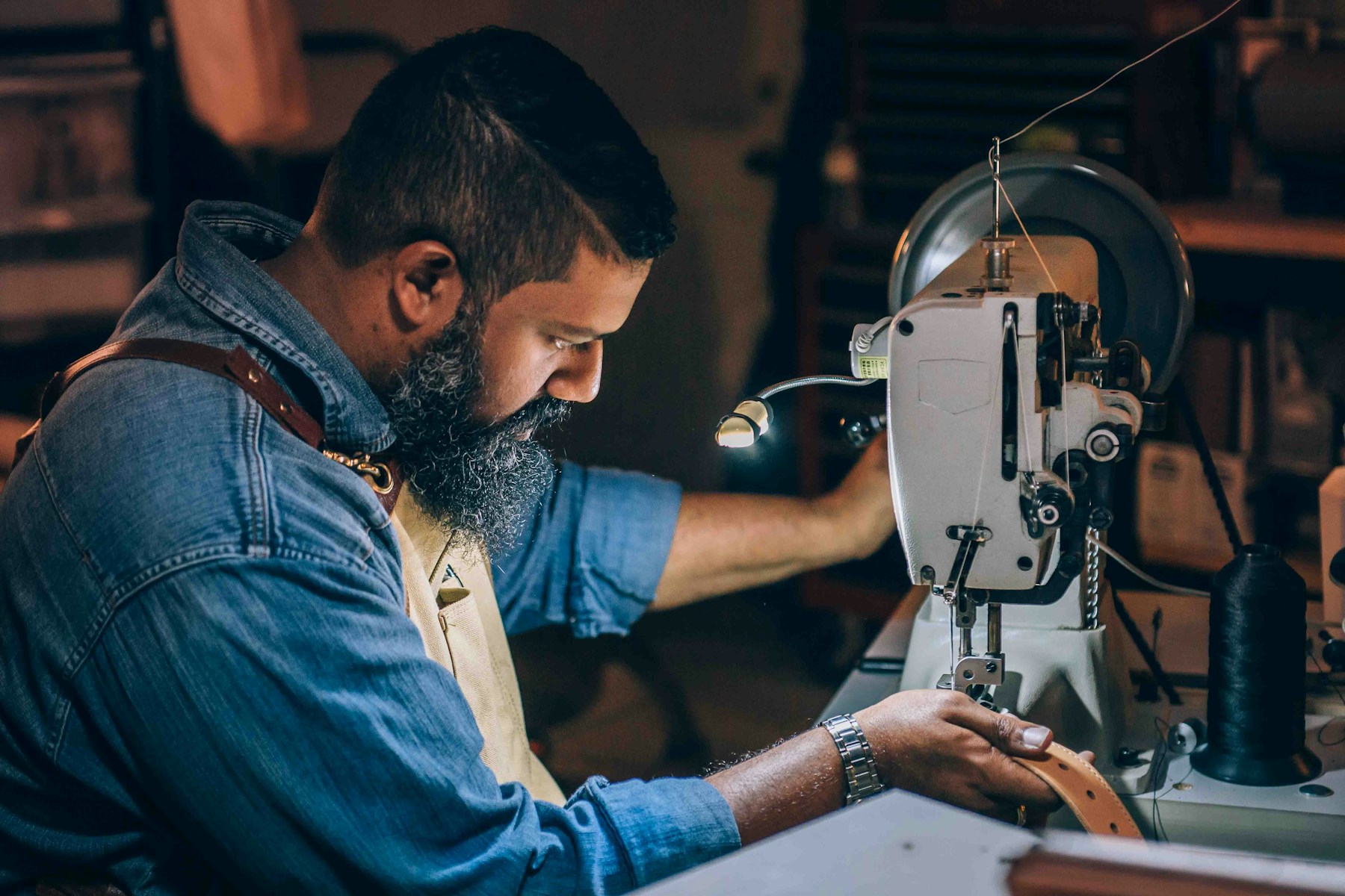 A craftsman stitching leather on an industrial post-bed sewing machine in a shoe workshop