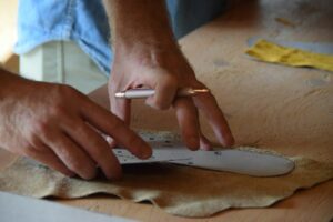 A shoe pattern being traced by hand onto a leather hide before cutting